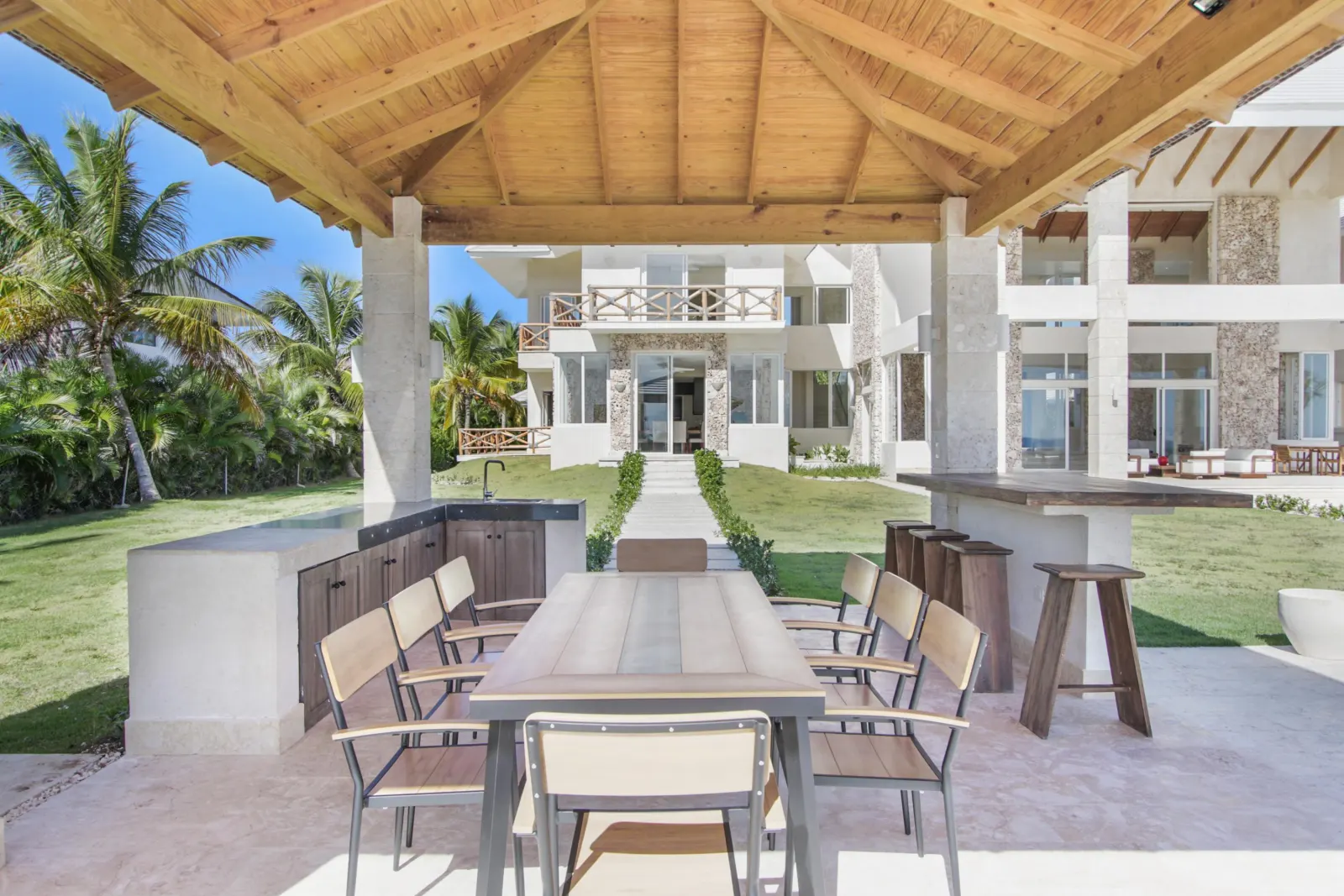 A table under a timber roof by the outdoor kitchen, the house beyond