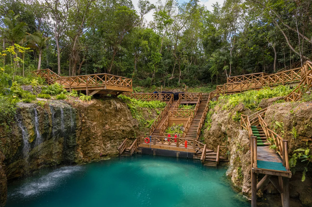 Hoyo Azul: a turquoise spring at the foot of a limestone wall, wooden stairs down through the forest