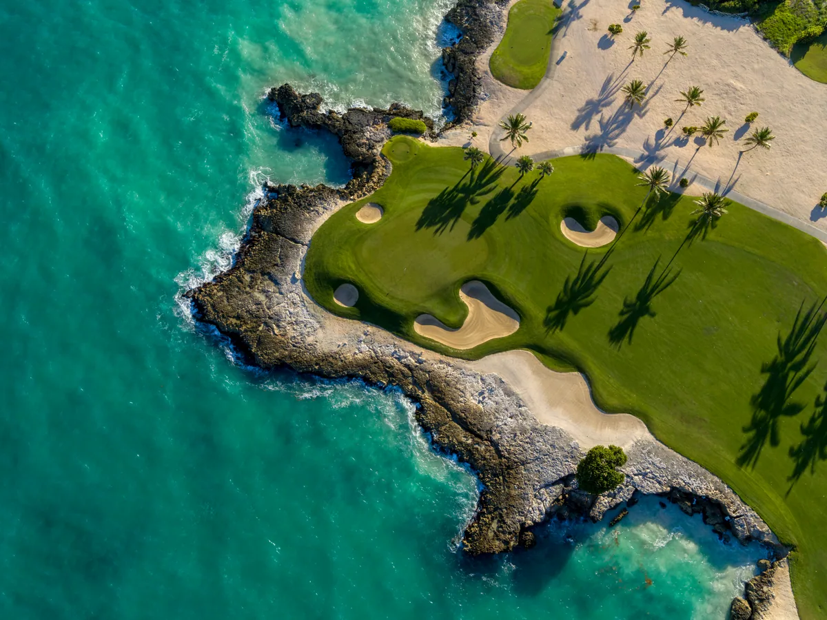 From above: a green on a peninsula of black rock in the turquoise sea