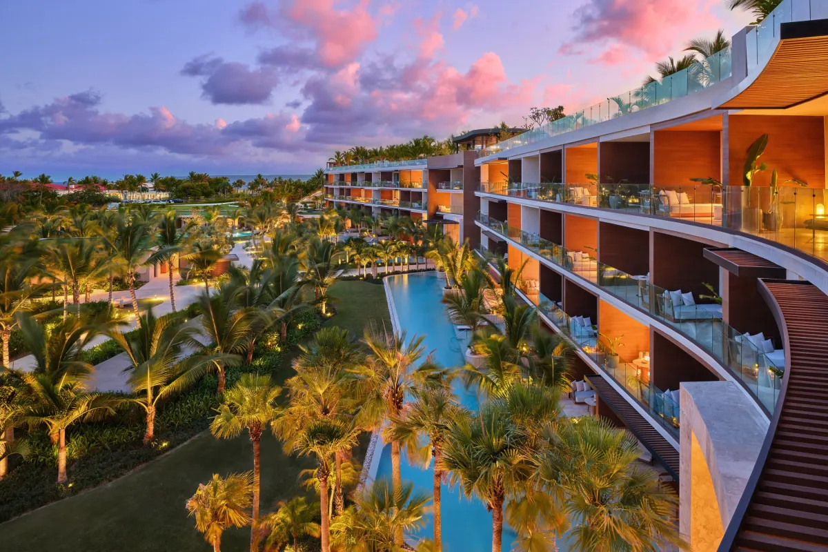 The curved façade of The St. Regis Cap Cana, terraces above a channel of water among the palms at dusk